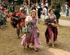 two women dressed in costume walking down a path with other people behind them and onlookers