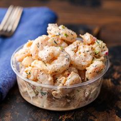 a glass bowl filled with shrimp salad on top of a wooden table next to a fork