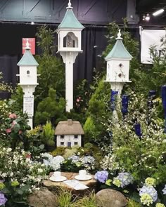 a garden with lots of different types of flowers and plants around it, including birdhouses