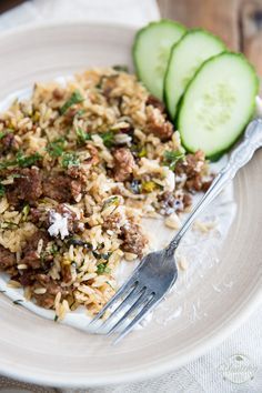 a white plate topped with rice and meat next to cucumbers