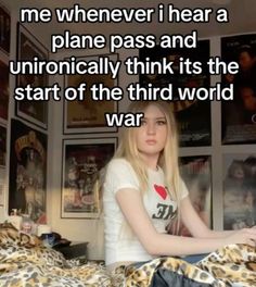 a woman sitting on top of a bed next to a wall with posters and pictures