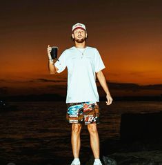 a man standing on top of a rock next to the ocean holding a cell phone