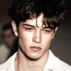 a close up of a person wearing a white shirt and looking at the camera with a serious look on his face