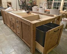 a kitchen island made out of wood with drawers and trash cans in the bottom drawer