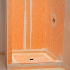 a bathroom with an orange wall and white tile on the shower walls, flooring is being installed