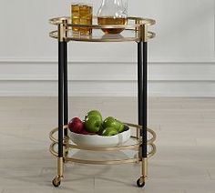 a gold and black bar cart with fruit on it in front of a white wall