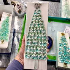 a person holding up a christmas tree made out of glass beads and other crafting supplies