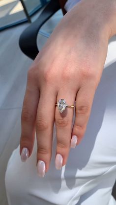 a woman's hand with a diamond ring on her left thumb and white nails