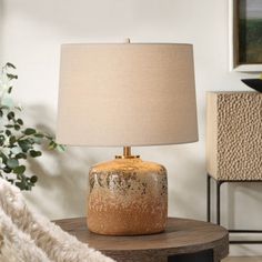 a table lamp sitting on top of a wooden table next to a white rug and potted plant