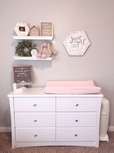 a baby's room with white furniture and pink accessories on the shelves above it