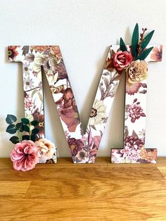 the letter m is decorated with flowers and leaves on top of a wooden shelf next to a wall