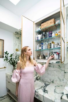 a woman in a pink dress is looking into a cabinet with many bottles on it