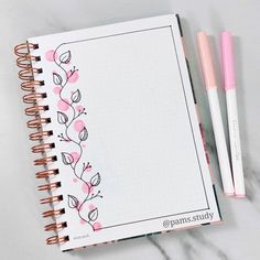 an open notebook with pink flowers on it and two pens sitting next to the page