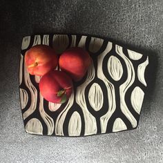 three apples and two oranges on a black and white platter with wavy designs