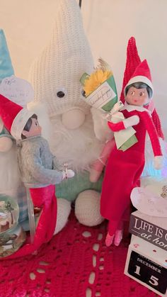 two elfs sitting next to each other near a teddy bear and snowman on a table