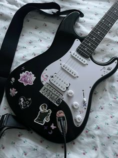 an electric guitar with many stickers on it laying on a bed next to a charger