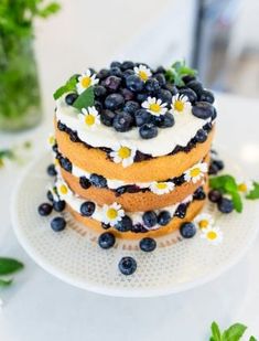 a three layer cake with blueberries and daisies on the top is sitting on a plate