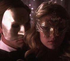 two people with masks on their faces in front of a curtain and lights behind them