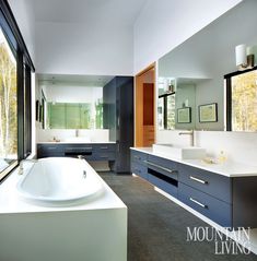 a large bathroom with two sinks and a bathtub next to a window that looks out onto the woods