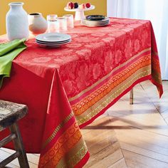 a red table cloth on a wooden chair with white vases and plates in the background