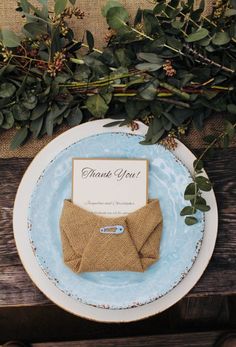 a blue and white plate with an envelope on it next to some greenery that says thank you