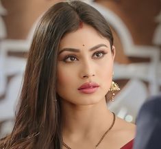 a woman with long brown hair wearing gold earrings and a red dress is looking at the camera