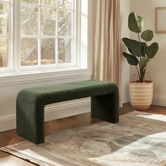 a green bench sitting in front of a window next to a rug and potted plant