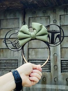 a hand is holding up a mickey mouse ears headband with a green bow on it