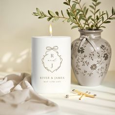 a white candle sitting next to a vase with a plant in it on a table