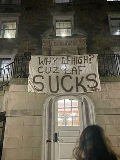 a woman standing in front of a building with a sign that says why high? cuzlaff sucks