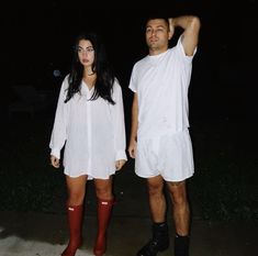 a man and woman dressed in white standing next to each other on the sidewalk at night