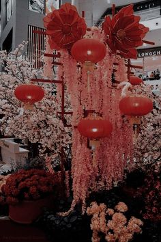 red lanterns hanging from the side of a tall building in front of trees and flowers