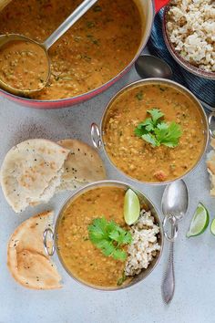 three bowls filled with soup next to some pita bread and cilantro wedges