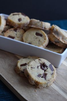 chocolate chip cookies sitting on top of a wooden cutting board next to a white dish