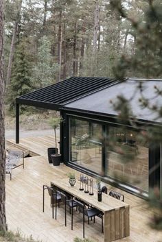 a wooden deck with tables and chairs in the woods next to a black metal roof