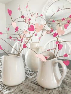 two white vases with pink paper hearts on them sitting on a table next to a mirror