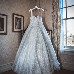 a wedding dress hanging on a hanger in front of a wall with pictures and curtains