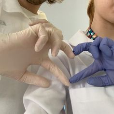 two people in white lab coats and blue gloves are doing something with their hands together