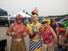 three men in colorful costumes standing next to each other at an outdoor music festival, one holding a ukulele