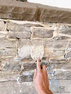 a hand is pointing at an exposed brick wall