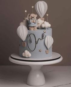 a blue cake decorated with hot air balloons and a teddy bear on top that says love