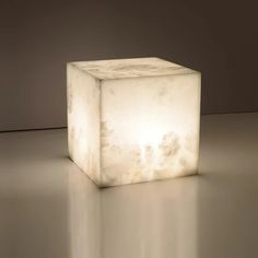 a white cube shaped light sitting on top of a gray floor next to a wall