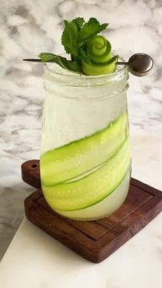 a glass filled with cucumber and mint on top of a cutting board