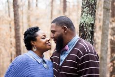 a man and woman standing next to each other in front of trees with their faces close together