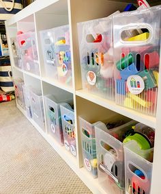 plastic storage bins filled with toys on top of a white book shelf in a room