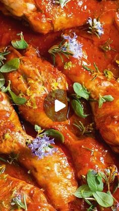 some chicken wings covered in sauce and garnished with fresh herbs, leaves and purple flowers