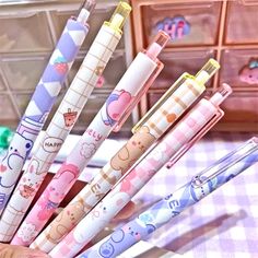 many different colored pens in a person's hand on a checkered tablecloth