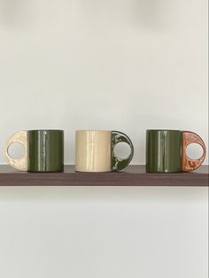 three coffee mugs are lined up on a shelf