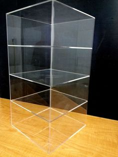 a clear acrylic display case sitting on top of a wooden table next to a black wall