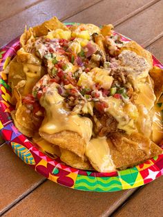 a colorful plate topped with nachos covered in cheese and toppings on top of a wooden table